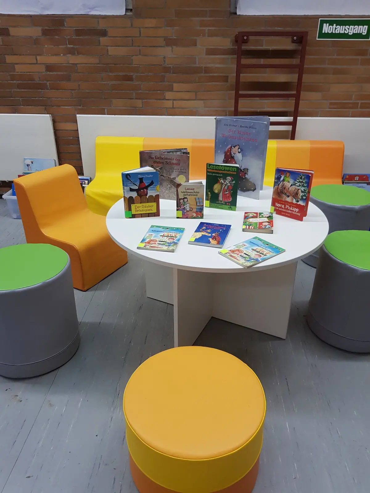 Eine bunte Sitzgruppe mit rundem Tisch und ausgelegten Kinderbüchern in der Bücherei