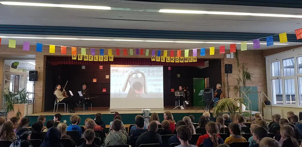 Kinder sitzen vor der Bühne, auf der Leinwand ist eine Zeichentrickfigur zu sehen