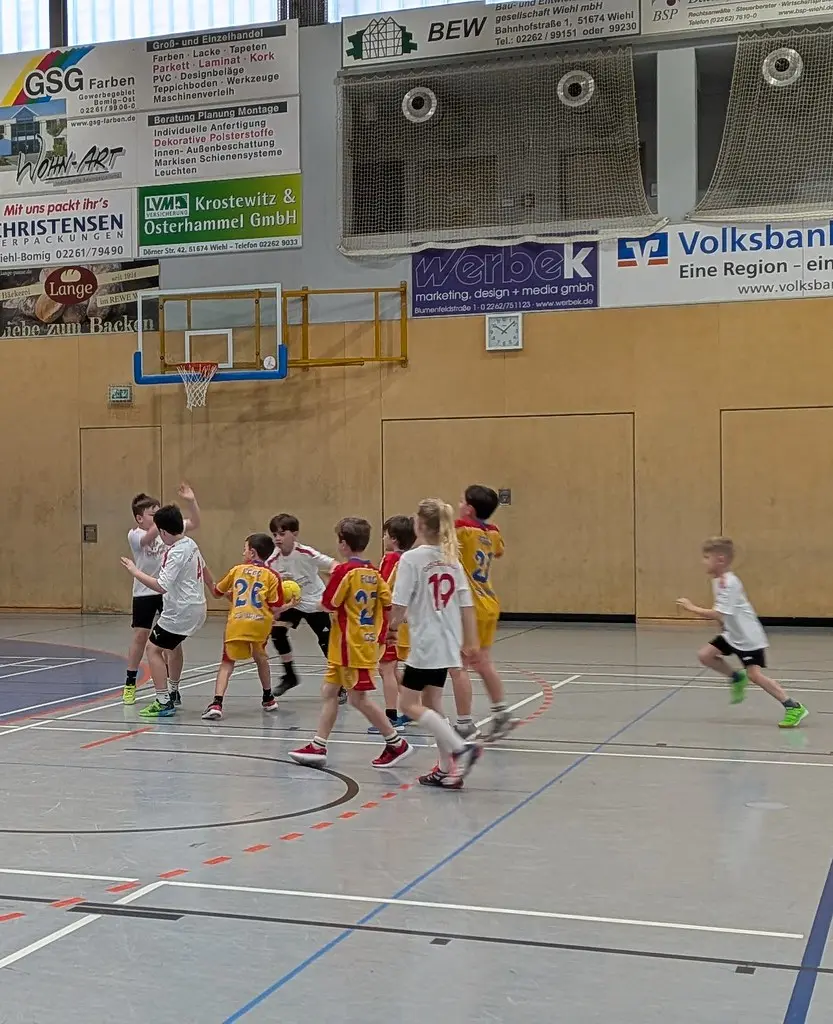 Spielszene in der Sporthalle, Kinder in Weiß und Gelb kämpfen um den Ball