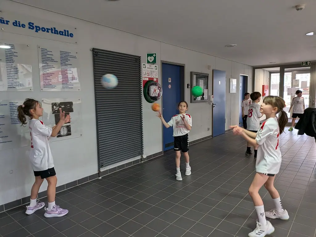 Kinder werfen sich im Hallenflur zum Aufwärmen Bälle zu