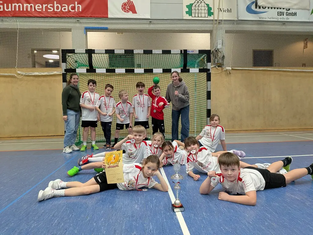 Mannschaft mit Medaillen, Pokal und Urkunde vor dem Handballtor