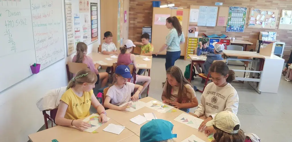 Kinder legen an Gruppentischen im Klassenraum Papierformen zusammen