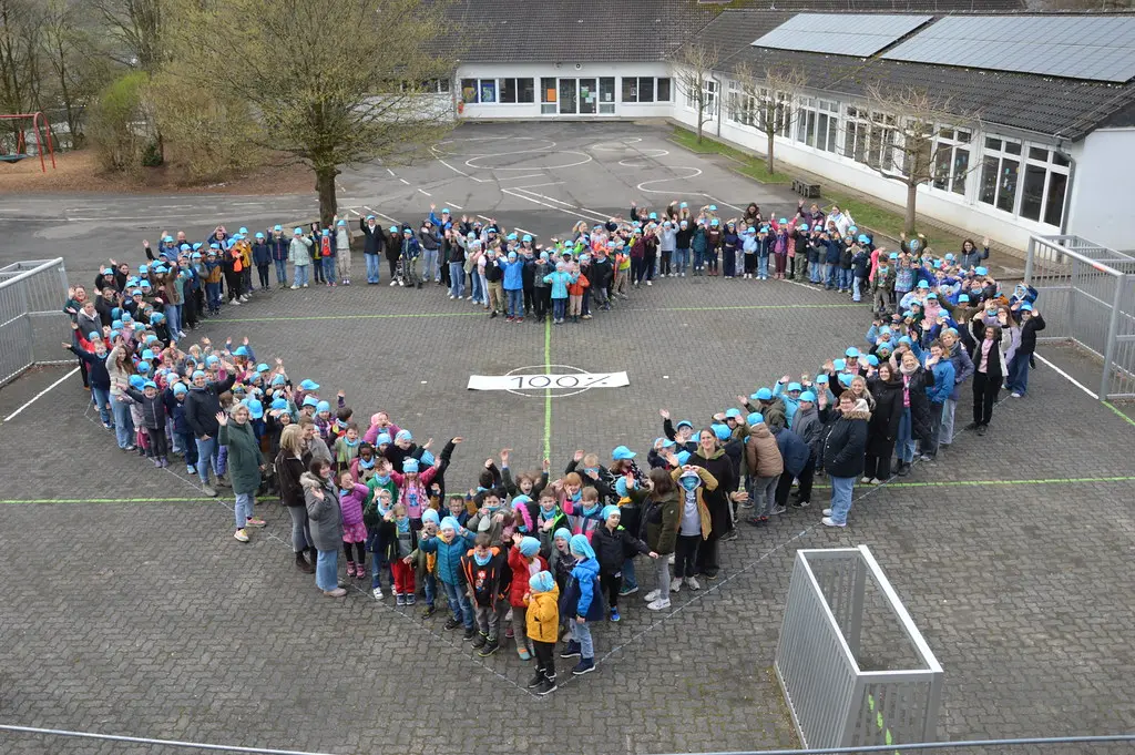 Schulkinder und Erwachsene stellen sich auf dem Schulhof zu einem großen Herz auf