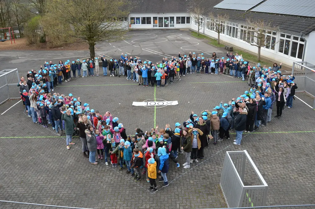 Herzformation aus Kindern und Erwachsenen rund um ein Banner mit 100 Prozent