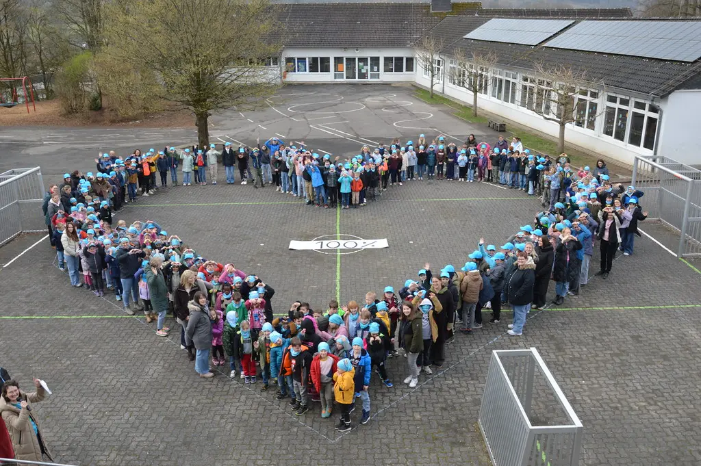 Blick von oben auf die Herzformation auf dem Schulhof, viele Arme winken