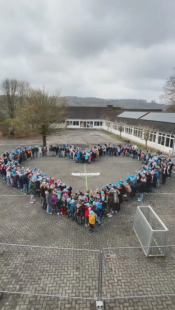 Weiter Blick über den Schulhof mit Herzformation unter bewölktem Himmel