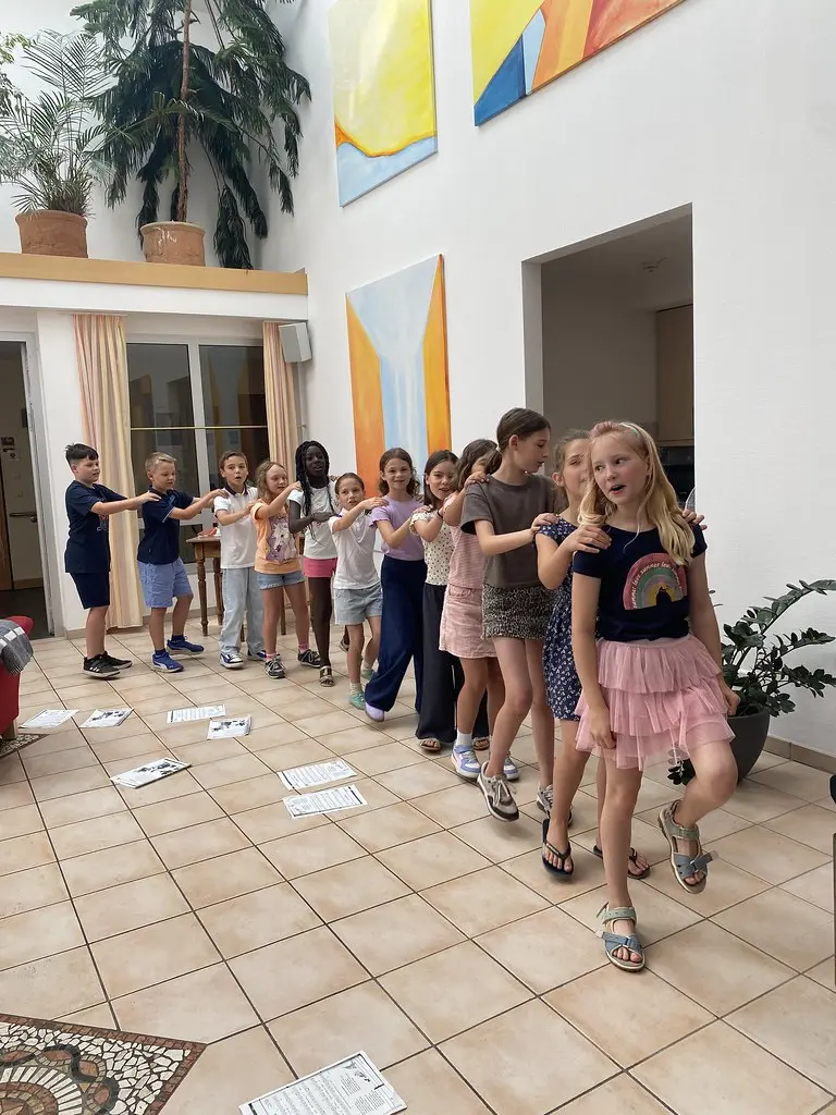 Kinder tanzen in einer Reihe durch das Atrium, die Hände auf den Schultern der Vorderleute