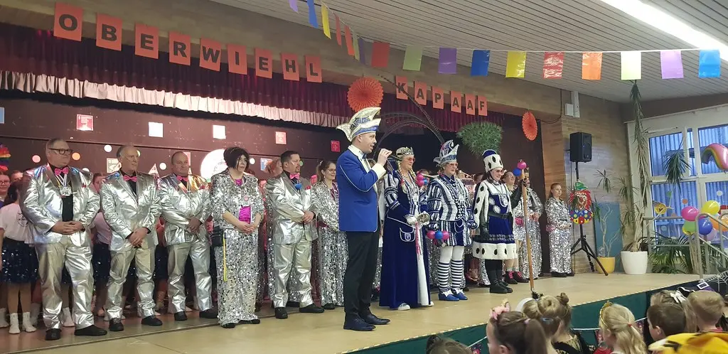 Karnevalsgesellschaft in Silberkostümen mit Prinzenpaar auf der Bühne unter dem Banner „Oberwiehl Kapaaf“