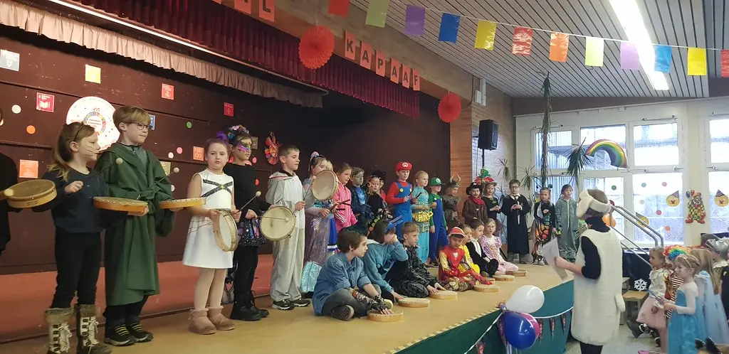 Verkleidete Kinder mit Trommeln und Tamburinen stehen und sitzen auf der Bühne