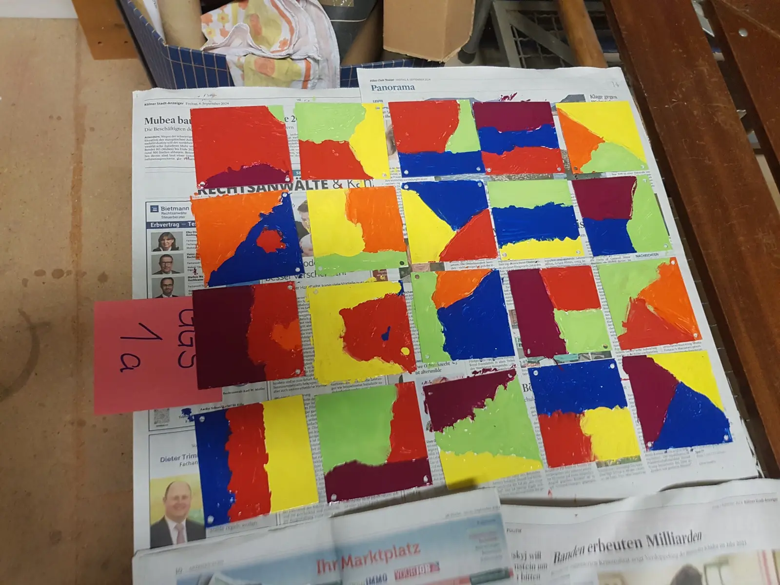 Bunt bemalte Farbfelder einer Klasse liegen zum Trocknen auf Zeitungspapier