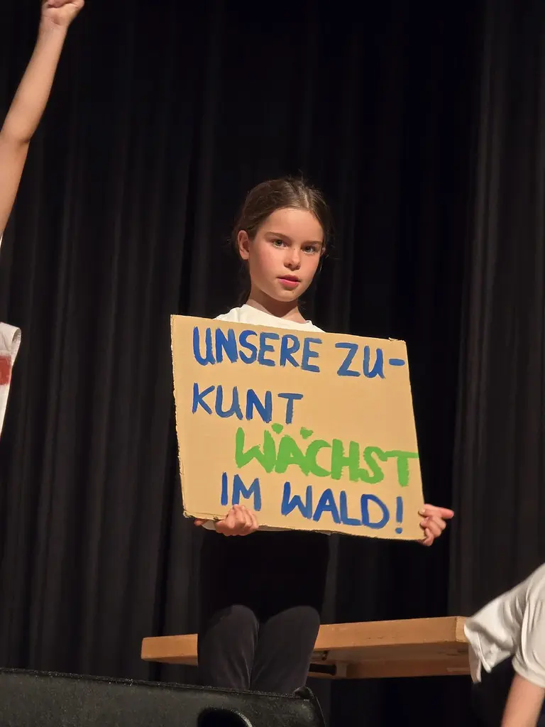 Ein Kind hält ein selbst gemaltes Schild mit der Aufschrift „Unsere Zukunft wächst im Wald!“