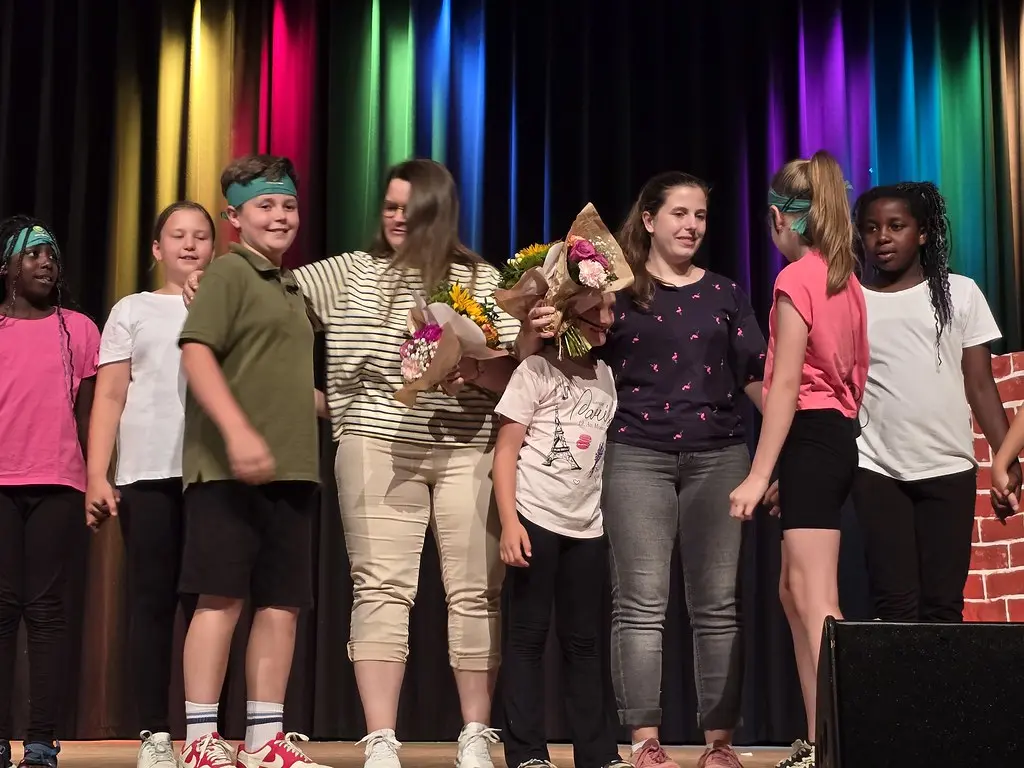 Kinder und zwei Erwachsene mit Blumensträußen beim Schlussapplaus auf der Bühne