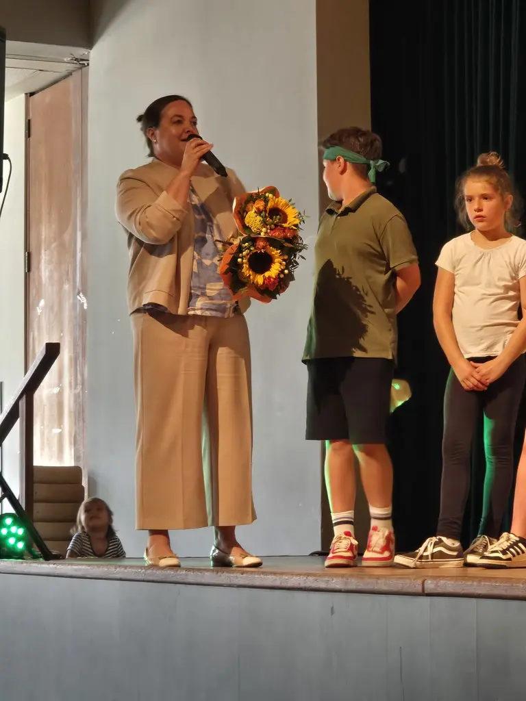 Eine Frau mit Mikrofon und Blumenstrauß dankt neben zwei Kindern auf der Bühne