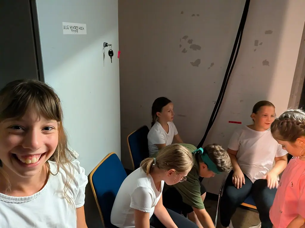 Kinder warten hinter der Bühne auf Stühlen, an der Wand ein Zettel „Alle Mikros hoch“