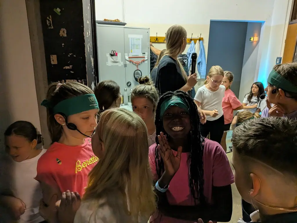 Kinder mit Stirnbändern und Headset-Mikrofonen drängen sich im Backstage-Raum