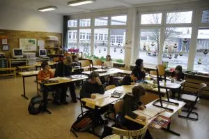 Kinder arbeiten an Einzeltischen im hellen Klassenraum an ihren Hausaufgaben