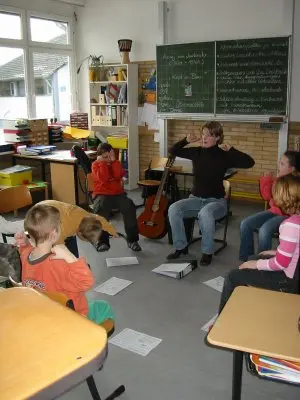 Die Musik-AG sitzt im Stuhlkreis, eine Betreuerin gibt vor der Tafel den Takt an