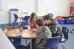 Drei Kinder spielen gemeinsam ein Brettspiel an einem runden Tisch