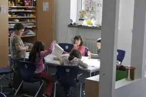 Kinder beschäftigen sich mit Papier und Stiften an Tischen im Gruppenraum