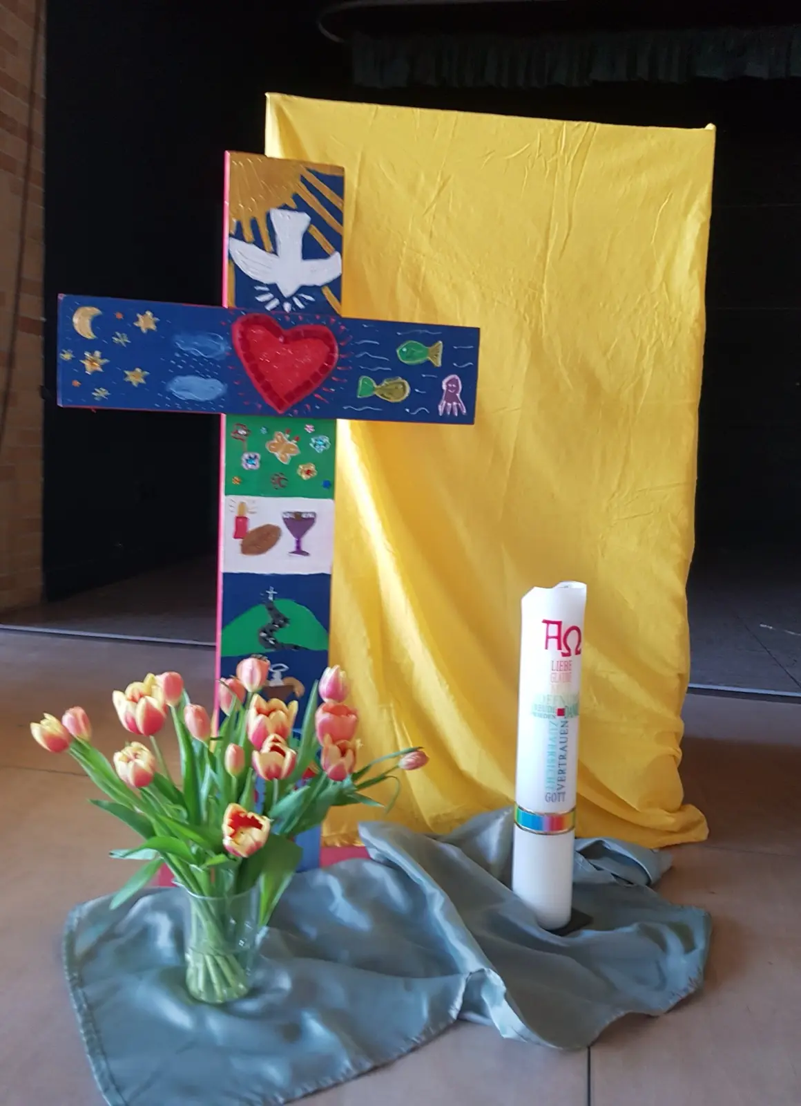 Von Kindern gestaltetes Holzkreuz mit Osterkerze und Tulpen als Gottesdienstaltar