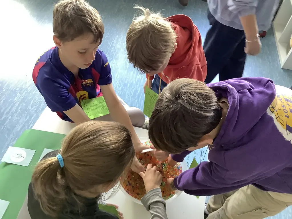 Mehrere Kinder untersuchen an einem Tisch eine Schale mit bunten Wasserperlen