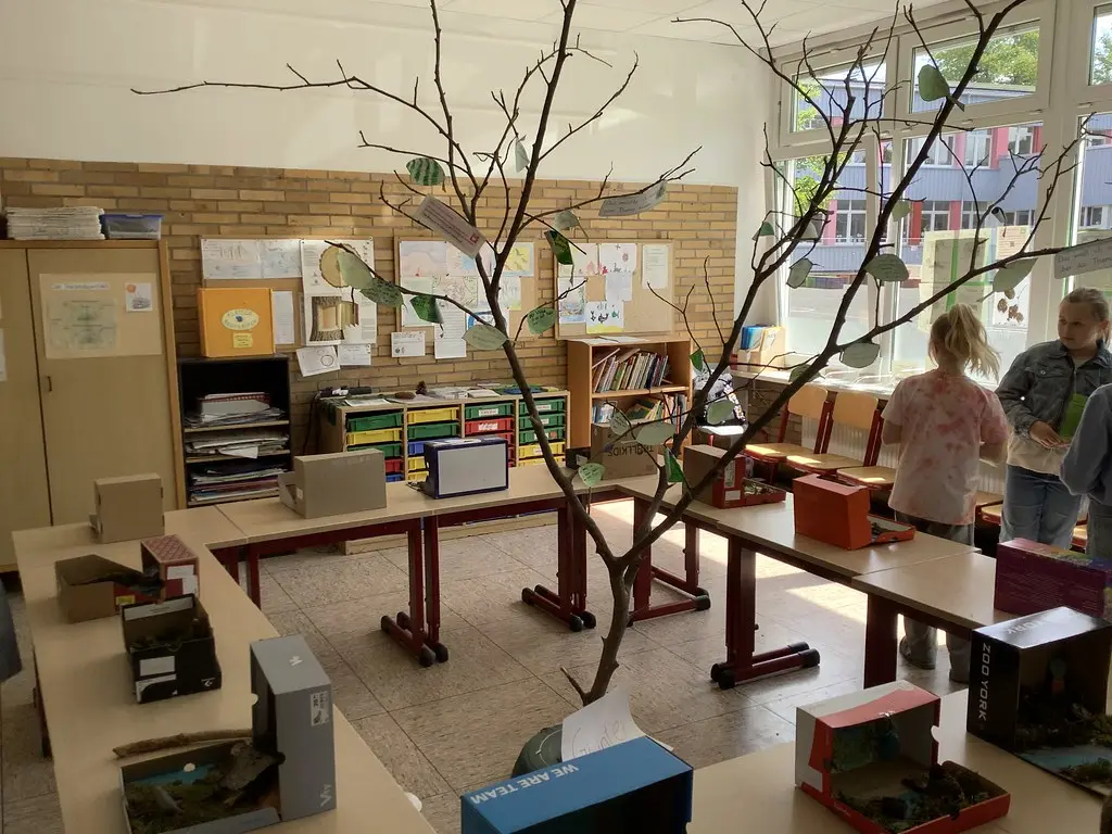 Klassenraum mit Deko-Ast, beschrifteten Blättern und Schuhkarton-Dioramen auf den Tischen