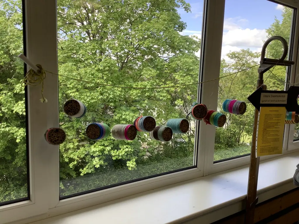Selbst gebaute Insektenhotels aus bunt umwickelten Dosen hängen vor einem Fenster