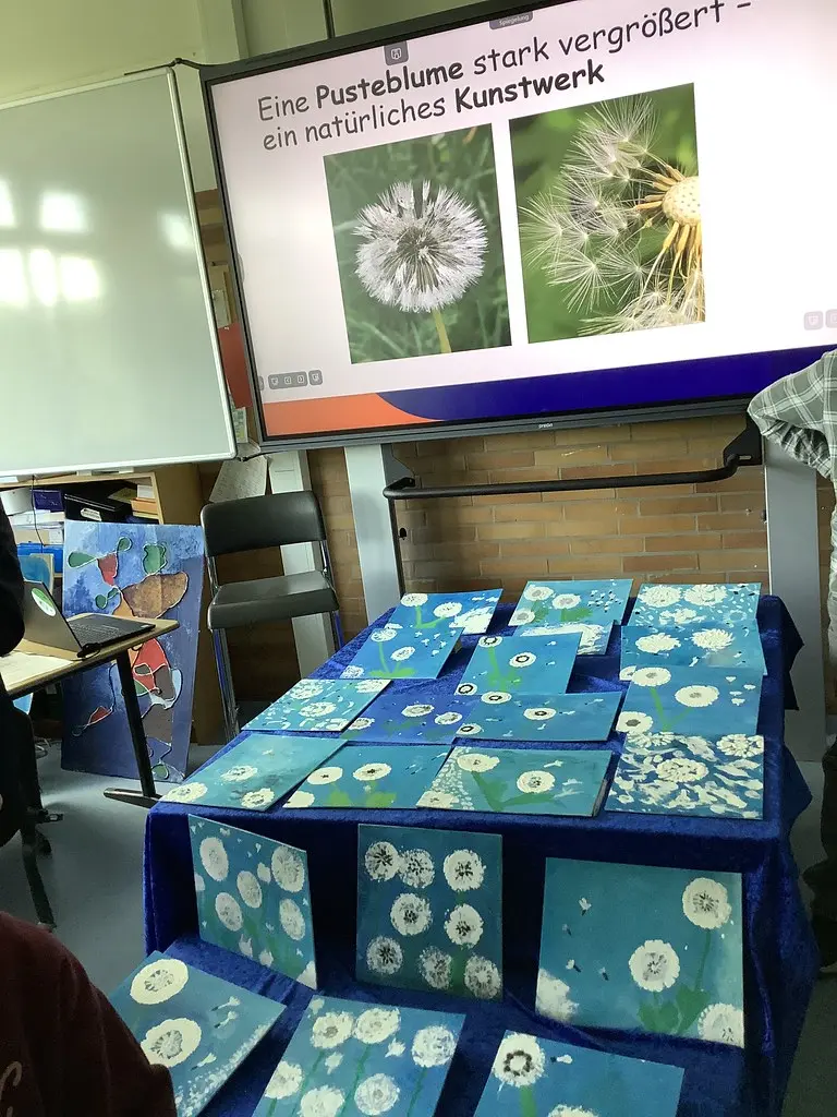 Gemalte Pusteblumen-Bilder auf einem Tisch vor einer Präsentation über Pusteblumen