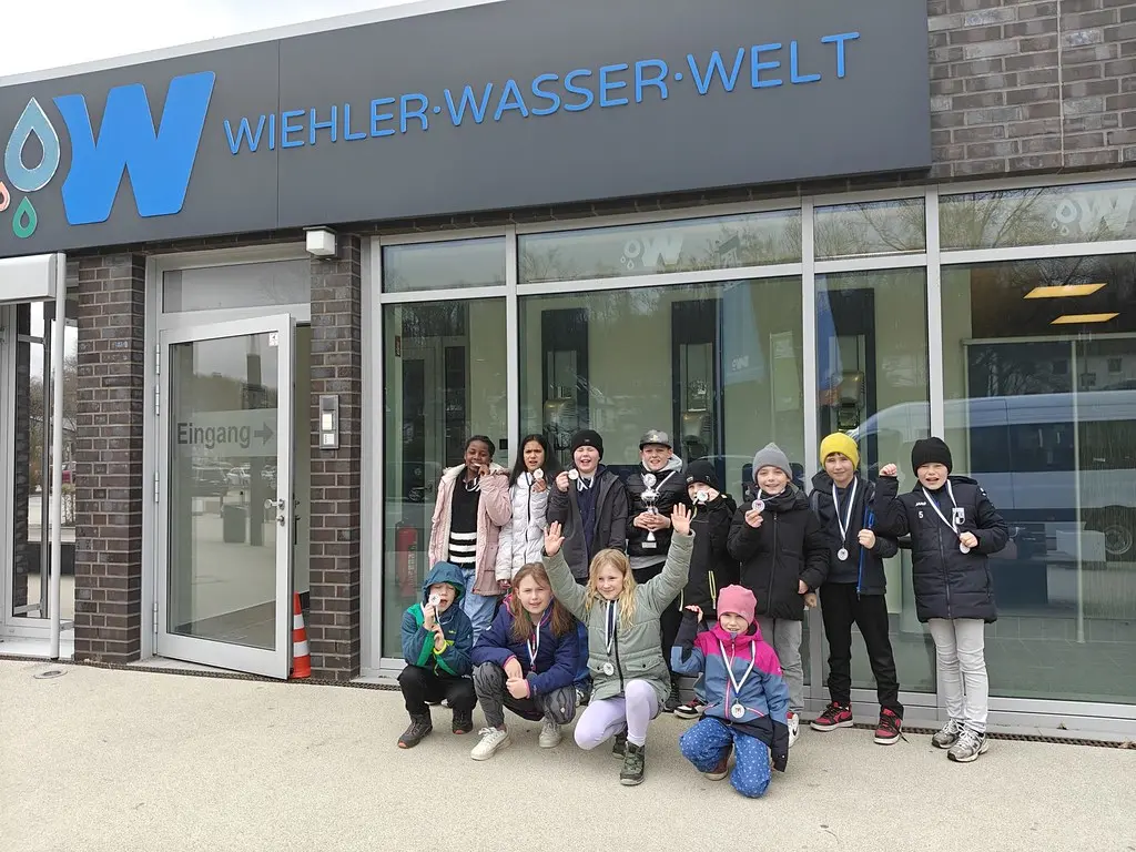 Winkende Kindergruppe mit Medaillen und Pokal vor dem Eingang der Wiehler Wasser-Welt